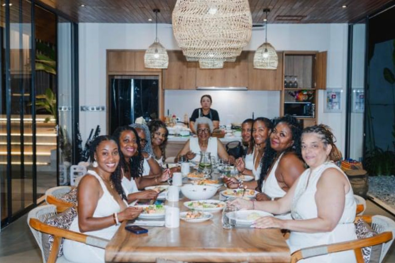 Women in white sharing dinner around a long table