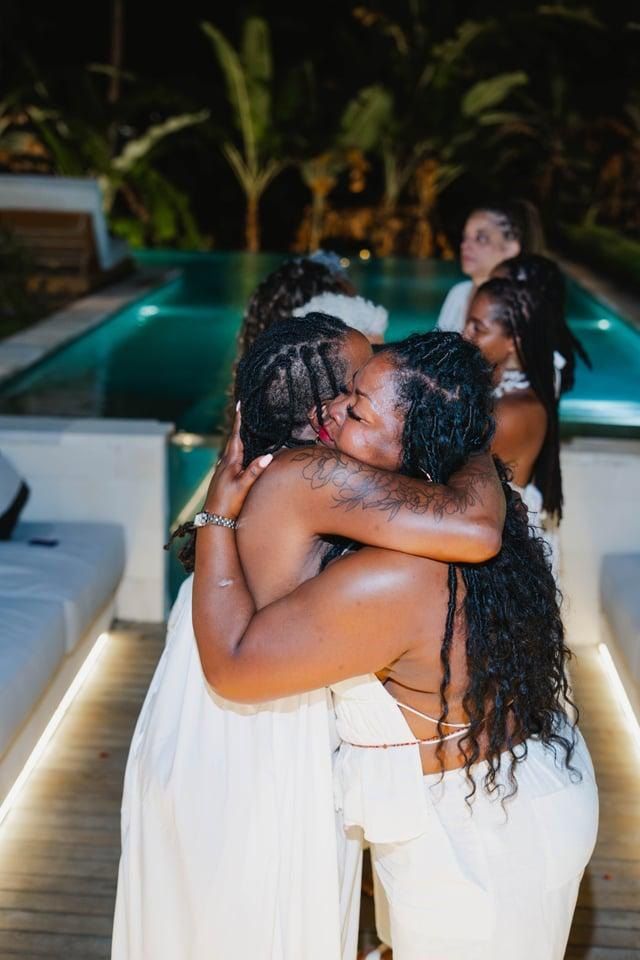 A warm embrace between two women in white by the pool at night