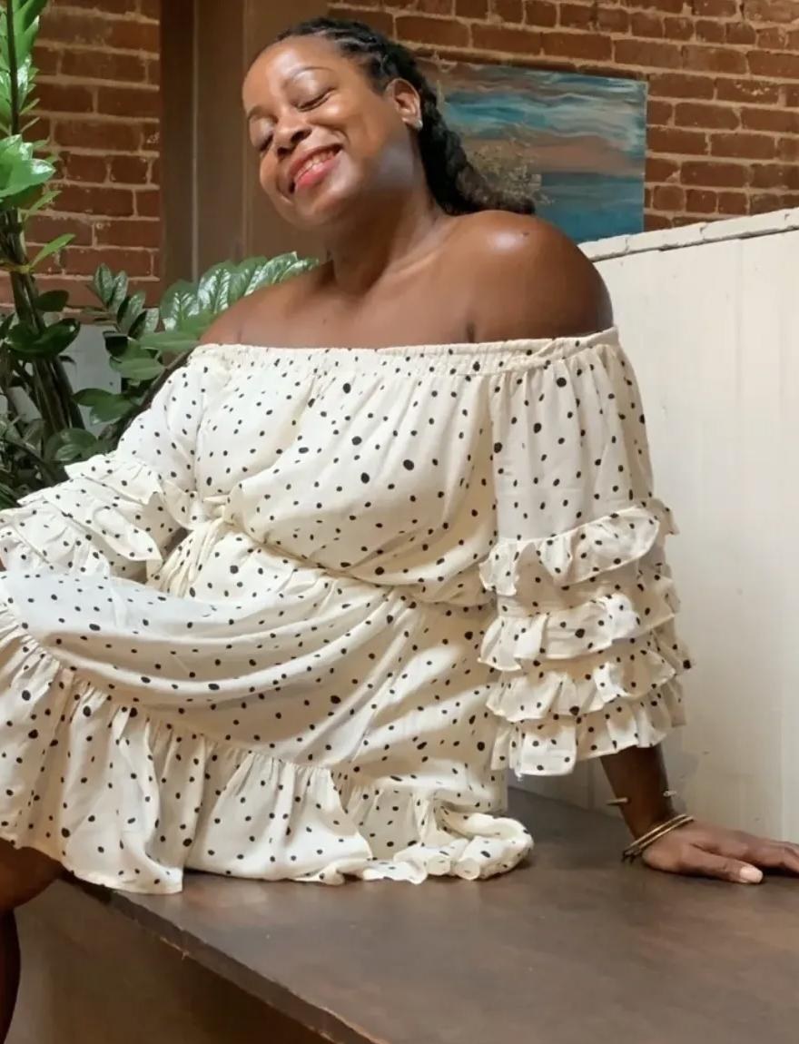 Terry smiling, seated in a white polka dot dress beside her plants