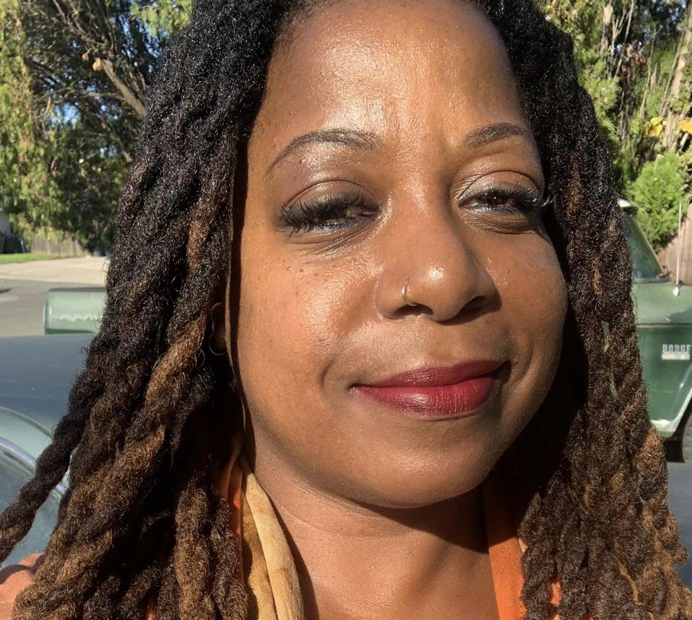 Terry outdoors in the sun, with long locs